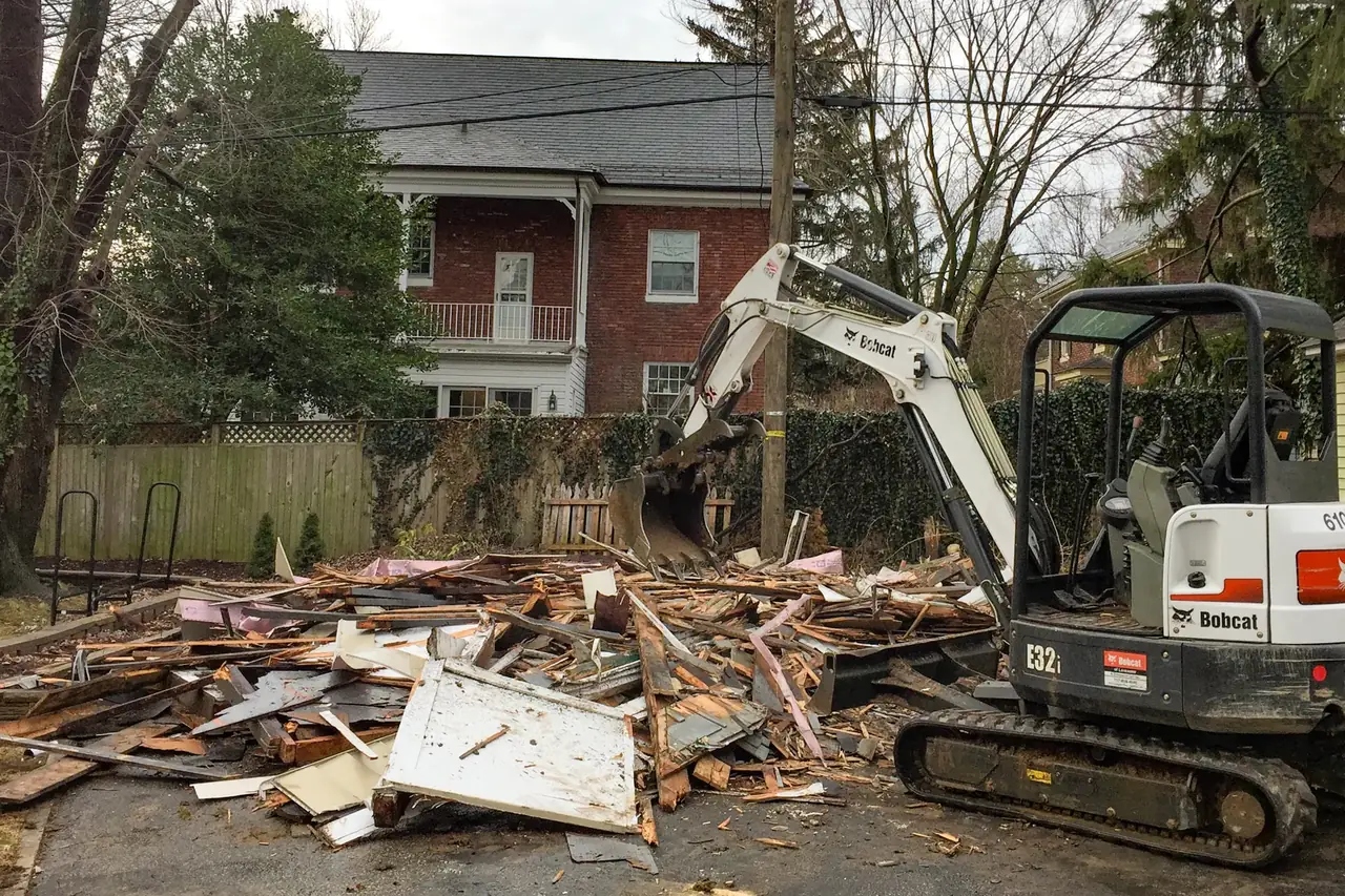 Mini excavator beside the wood debris of a torn-down backyard building