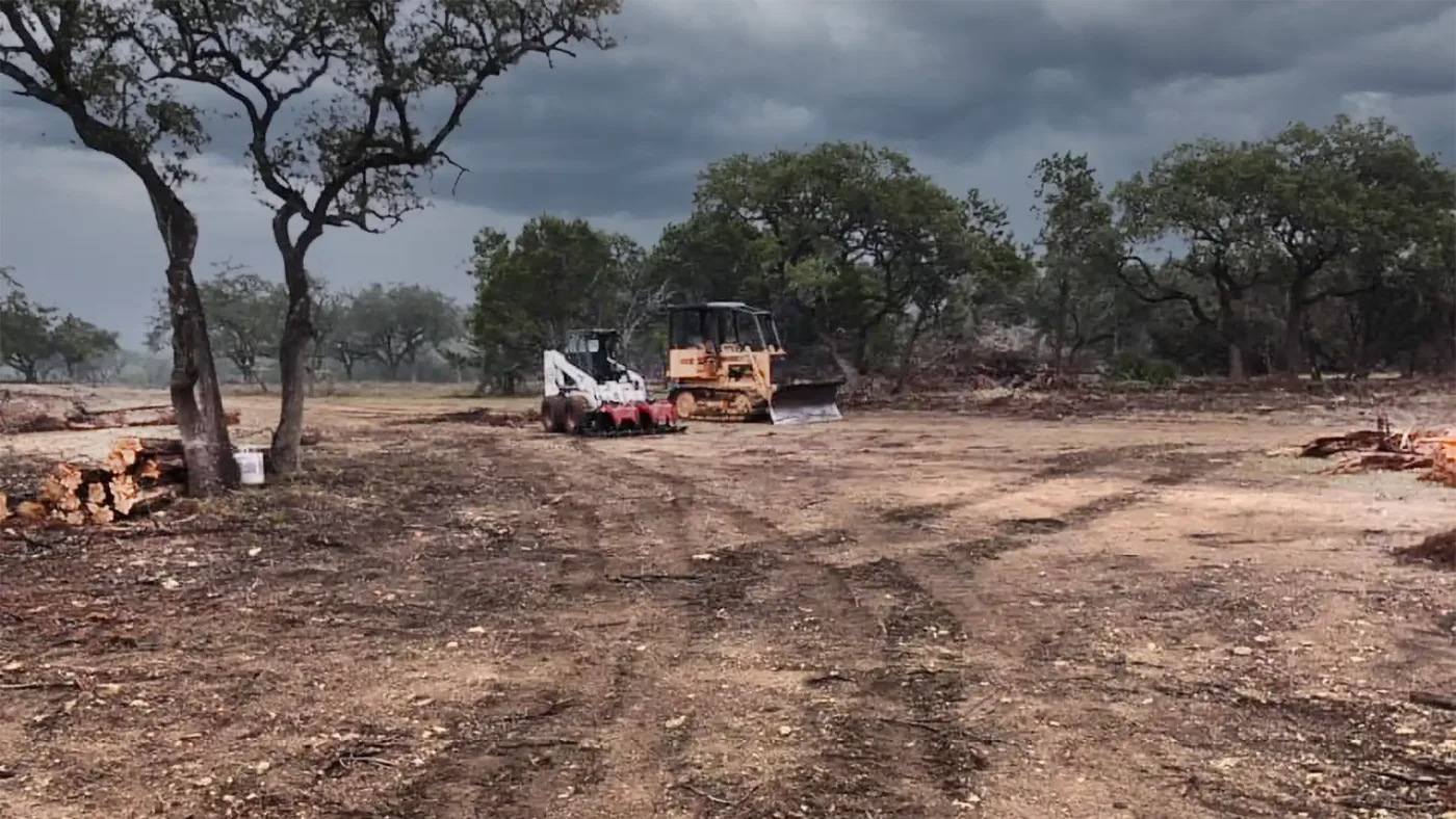 Cleared lot with a dozer and skid steer parked among the oaks that were kept