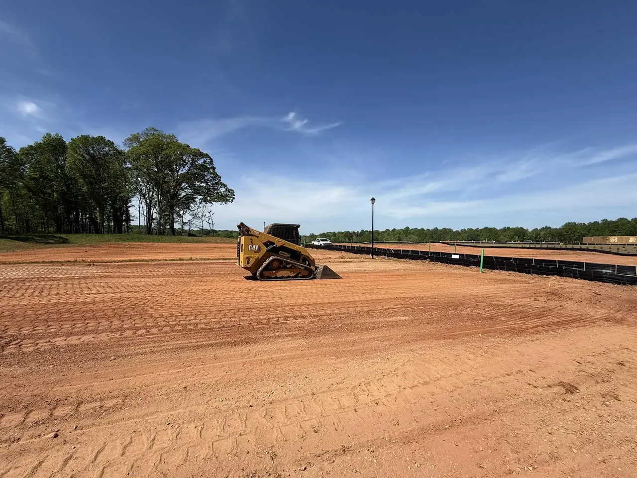 CAT compact track loader on a freshly graded red clay building pad with silt fence along one edge